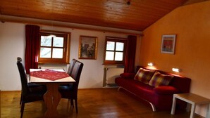 Een gezellige kamer met een houten plafond, een eettafel met stoelen, een rode bank en een klein wit tafeltje.