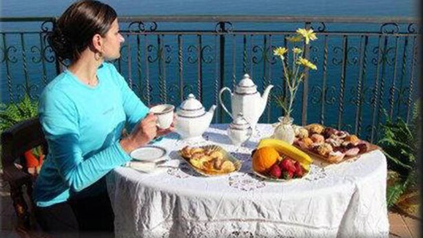 A table set with tea, a teapot, and various pastries and fruits, with a view of the sea in the background. - B&B Casa Armonia (Pizzo)