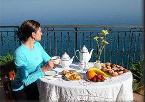 A table set with tea, a teapot, and various pastries and fruits, with a view of the sea in the background. - B&B Casa Armonia (Pizzo)