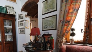 A cozy room with a wooden cabinet, a round table with books and bottles, a red lamp, and framed maps on the wall. - B&B Casa Armonia (Pizzo)