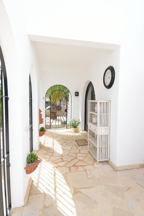 A hallway with a stone floor, white walls, and a gate leading to a garden. - Sea view, close to the beach, quiet location, private pool, air conditioning, internet, ecological (Cala Murada)