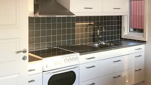 Une cuisine avec des armoires blanches, un dosseret en carreaux noirs, un évier en acier inoxydable et un four encastré.