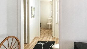 Un couloir avec un plancher en bois, un tapis noir et blanc, une chaise blanche et une chaise en bois.
