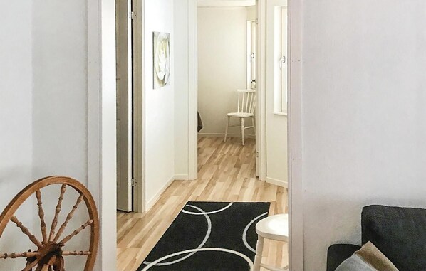 A hallway with a wooden floor, a black and white rug, a white chair, and a wooden chair.