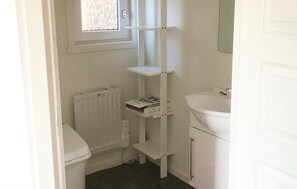 A small, white bathroom with a toilet, a radiator, a shelf unit, and a sink. - Cozy home in Vena with house sea view (Vena)