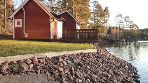 Une cabane avec une terrasse en bois et un mur en pierre, située au bord d’un lac.