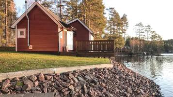 Une cabane avec une terrasse en bois et un mur en pierre, située au bord d’un lac.