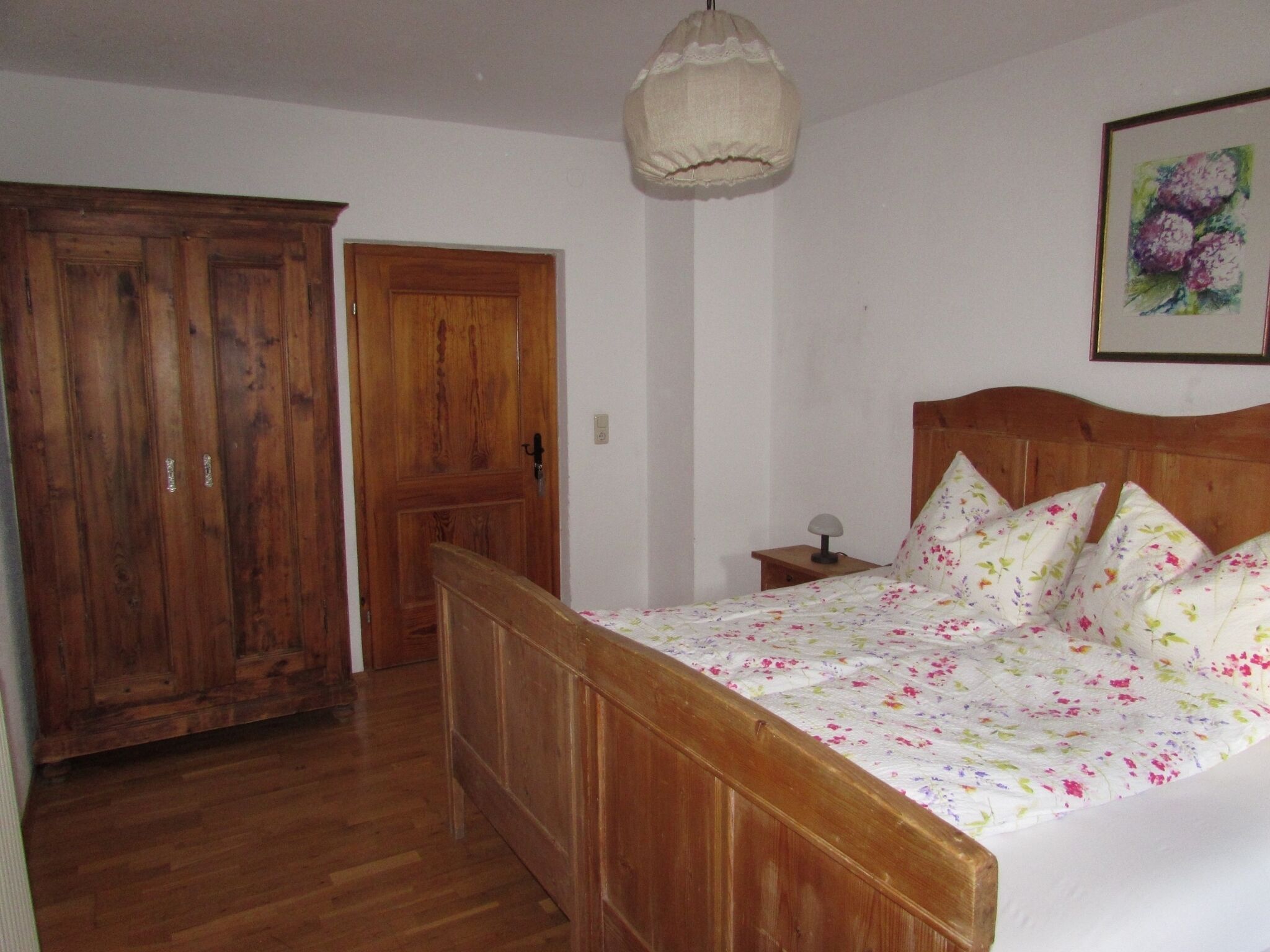 Une chambre avec un lit en bois, une table de chevet, une lampe suspendue et une porte.