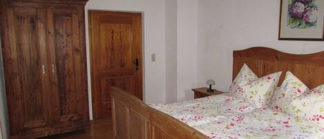 A bedroom with a wooden bed, a nightstand, a hanging light, and a door.