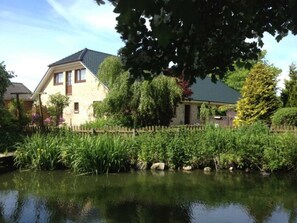 Een huis met een gevel van natuursteen, een schuin dak en een houten omheining rond een vijver.