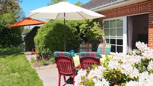 A patio with outdoor furniture, a white umbrella, and blooming flowers.