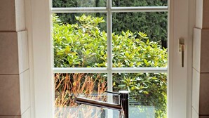 A kitchen with a stainless steel sink and a modern faucet, a window with a view of greenery, and a door with a handle.