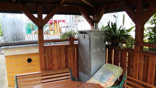 Une terrasse en bois avec une table et des bancs, un barbecue en métal et des plantes en pot.