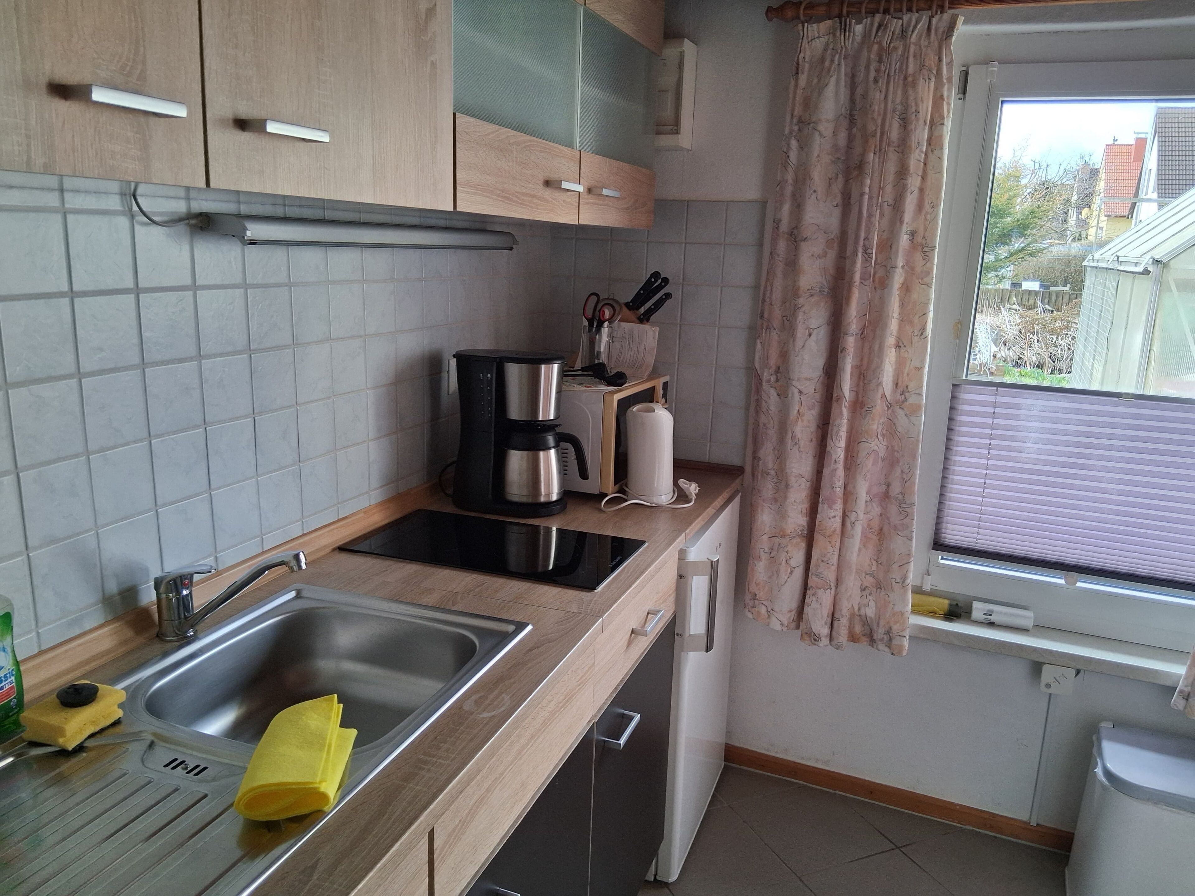 Una cocina moderna con un lavamanos, cafetera y ventana con cortinas.