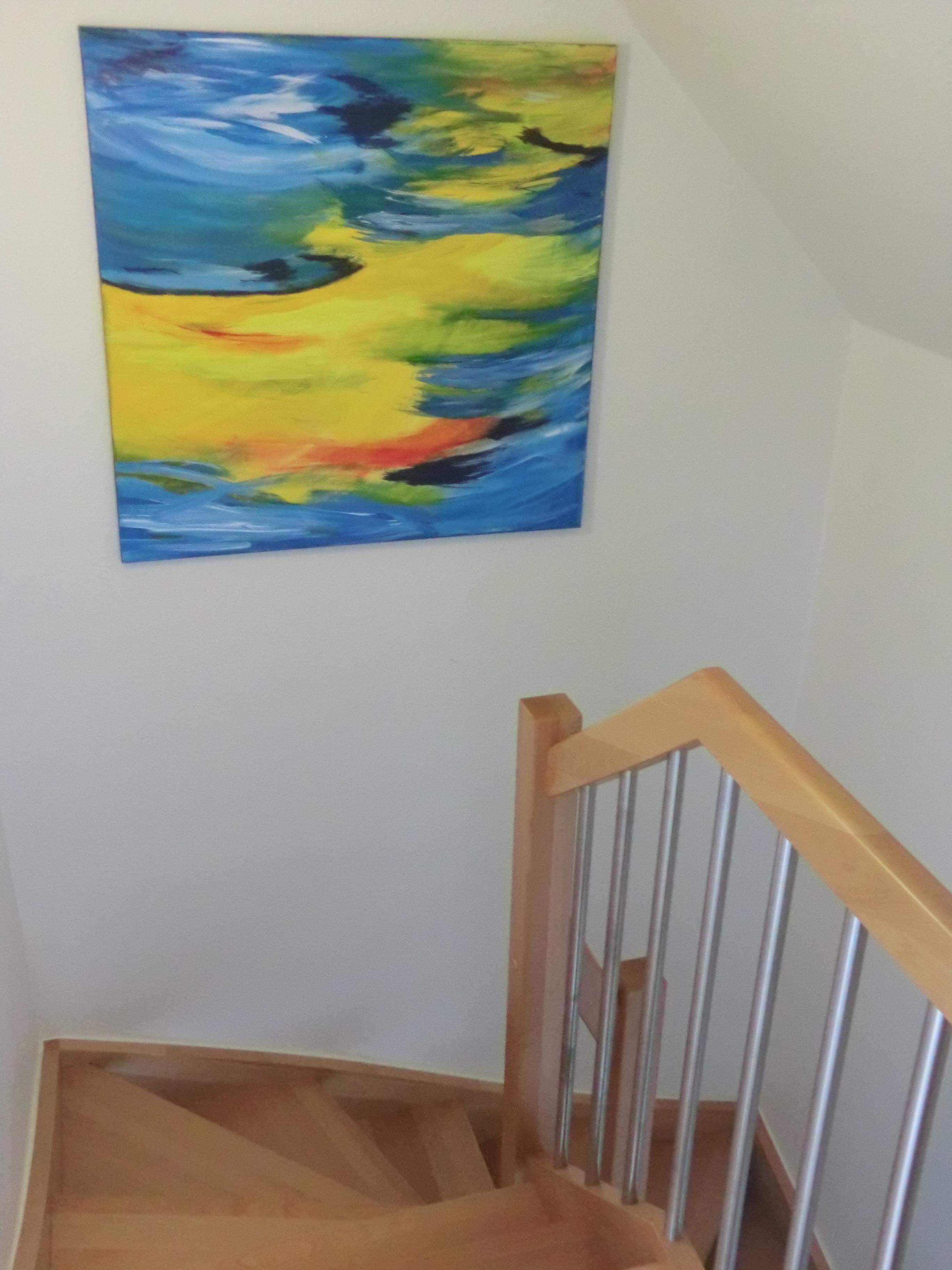Eine Treppe mit hölzernen Geländern und einem farbenfrohen, abstrakten Gemälde an der darüberliegenden Wand.