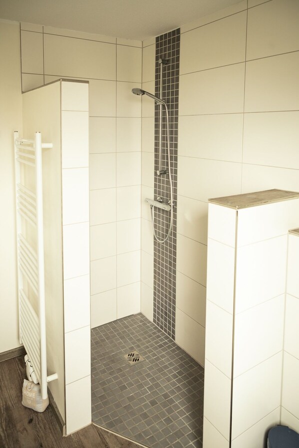 Un espacio de ducha pequeño y cerrado, con pared y suelo de baldosas, un perchero blanco y un pequeño contenedor para guardar objetos.
