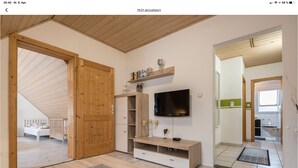 Une chambre moderne avec un plafond en bois, un lit, une télévision et un petit coin cuisine.