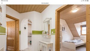 Une chambre moderne et bien éclairée, située sous les combles, avec un plafond en pente, une petite fenêtre et une porte en bois.