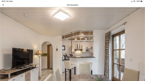 Un salon moderne doté d’un téléviseur à écran plat, d’un coin repas avec des chaises, d’une cuisine avec des placards et d’une grande fenêtre.