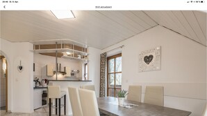 Une cuisine moderne avec des meubles blancs, un four encastré et un coin repas comprenant une longue table et des chaises.