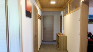 Un couloir avec des plafonds et des murs en bois, un sol carrelé et un banc surmonté d’un tapis à motifs.