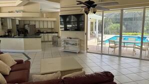 Un vaste espace de vie comprenant un canapé, une table basse et une vue sur une piscine, grâce à de grandes portes-fenêtres coulissantes.
