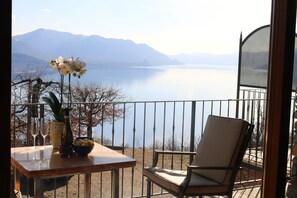 Un balcone con tavolo, una sedia e vista su un lago con montagne sullo sfondo.