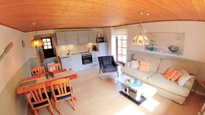 Un vaste espace de vie doté d’un plafond en bois, d’une table à manger avec des chaises, d’un canapé et d’une cuisine à l’arrière-plan.