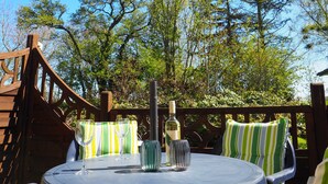 Une terrasse en bois avec une table ronde, des coussins verts et blancs à rayures, et une bouteille de vin.