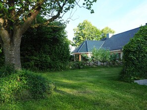 Uma casa com telhado inclinado, rodeada por um gramado bem cuidado e vegetação densa.