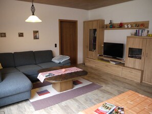 Una sala de estar con un sofá, una mesa de centro, un televisor, armarios de madera y una lámpara colgante.