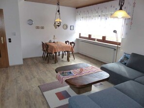 A living room with a sofa, a dining table with chairs, a coffee table, and a window with curtains.