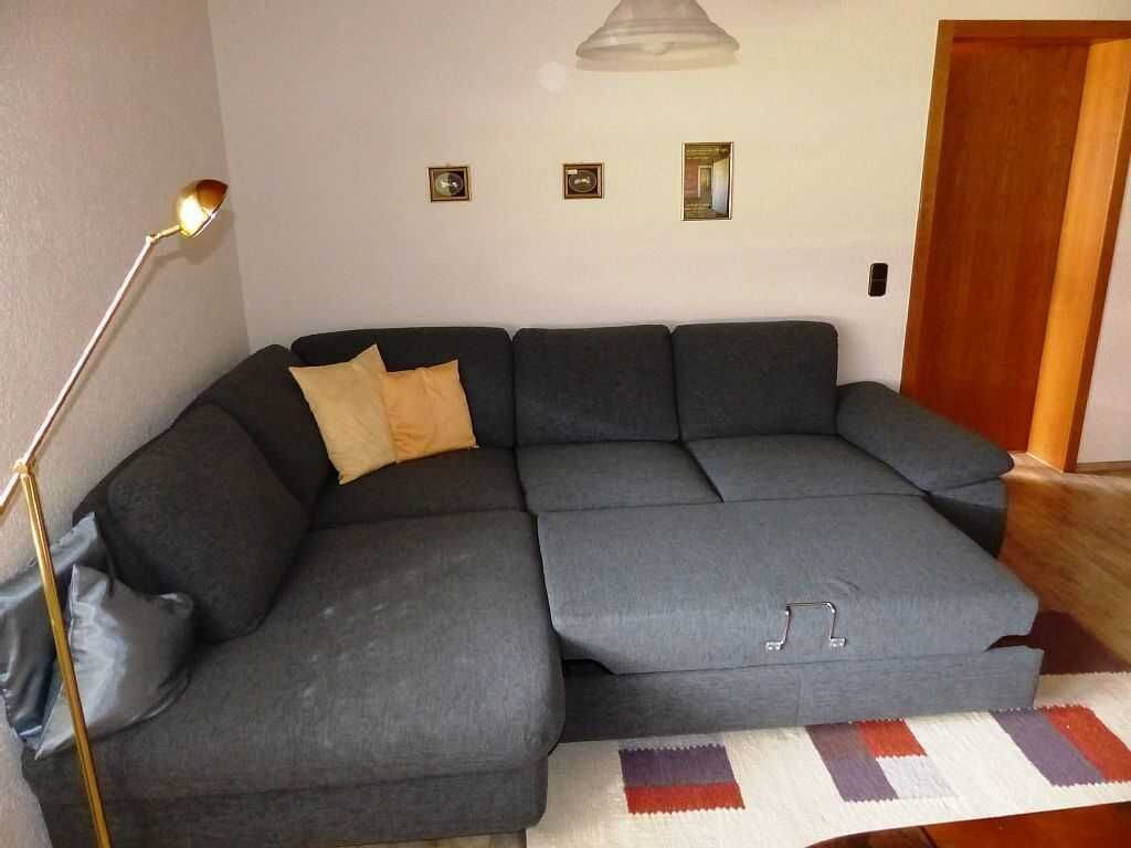 Un sofá modular con una lámpara colgante, una alfombra pequeña y una puerta de madera.