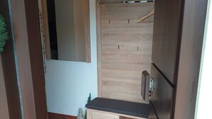 Una habitación pequeña con suelo de baldosas, un armario de madera, un banco y una percha.