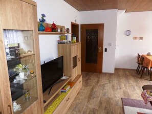 A living room with a TV, wooden cabinets, a dining table, and a door.