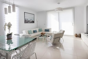 A modern living room with a glass dining table, white sofa, and metal chairs.