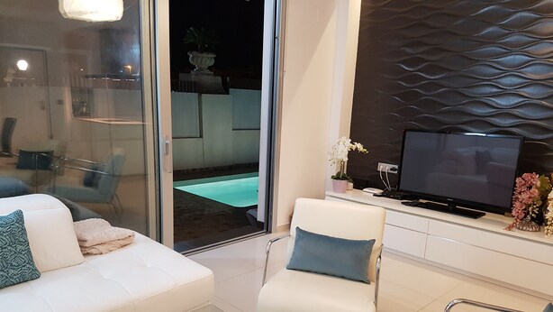 Una sala de estar moderna con un sofá blanco, una mesa de centro de vidrio y un televisor sobre un mueble blanco.