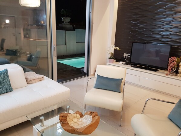 Una sala de estar moderna con un sofá blanco, una mesa de centro de vidrio y un televisor sobre un mueble blanco.