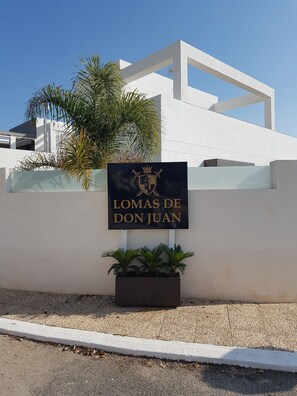 A sign with "Lomas de Don Juan" written on it, placed in front of a white building with a modern design, accompanied by a potted plant.