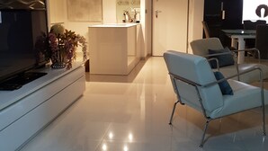 Una sala de estar moderna con un televisor de pantalla plana, un sofá blanco y una cocina al fondo.