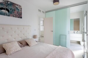 Quarto com uma cama grande, mesa de cabeceira, abajur e uma pintura de uma ponte.