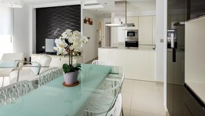 Cocina moderna con electrodomésticos de acero inoxidable, una mesa de vidrio y una orquídea en maceta, además de una silla blanca.
