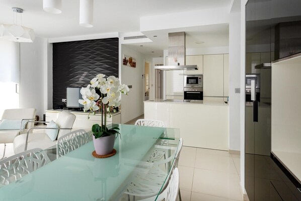Eine moderne Küche mit Edelstahlgeräten, einem Glastisch mit Orchidee im Topf und einem weißen Stuhl.