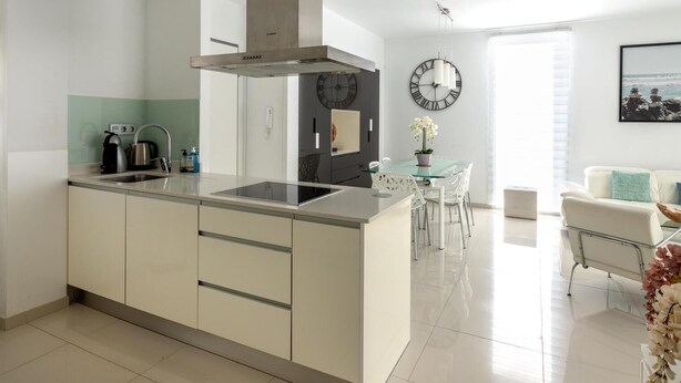 Una cocina moderna con una isla central, estufa integrada y un reloj grande en la pared.