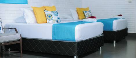 Dos camas con ropa de cama blanca y azul, una persiana azul y una pared de ladrillo blanco.