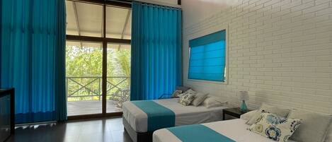 Una habitación de hotel moderna con dos camas, un ventanal con cortinas azules, una pared de ladrillo blanco y un techo con vigas a la vista.