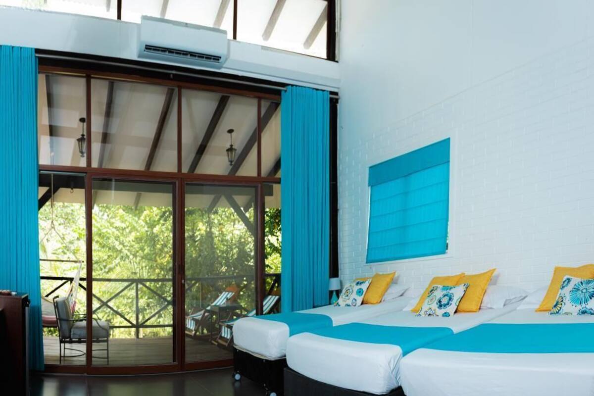A bedroom with two beds, a large sliding glass door leading to an outdoor area, and a white brick wall.