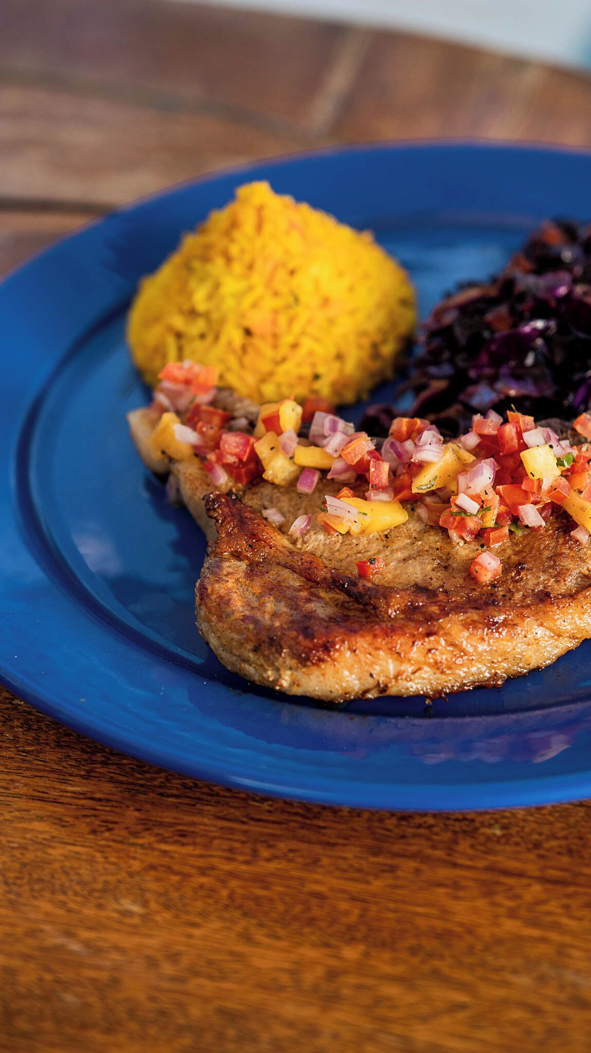 A plate with a grilled pork chop, yellow rice, and a side of red cabbage.