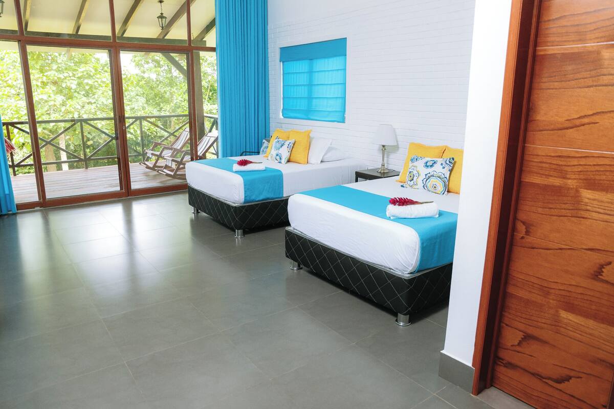 A hotel room with two beds, a large window, and a balcony.