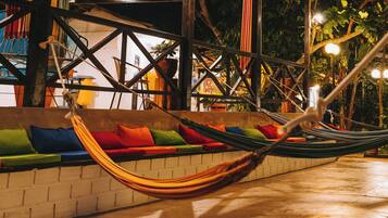 A hammock under a roofed area with colorful cushions and a brick wall.